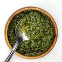 Skinny pesto in a wooden bowl with olive oil and a spoon.