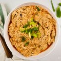 Slow cooker buffalo chicken shredded in a bowl with diced celery and buffalo sauce.