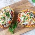 Spaghetti squash burrito bowls with beans, peppers, onions, seasoning, and melted cheese on a cutting board.