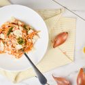 One pot spinach tomato pasta in a bowl with Parmesan cheesee with a napkin and shallots.