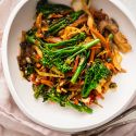 Stir fried vegetables with cabbage, mushrooms, broccoli, and carrots in stir fry sauce in a white bowl.