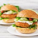 Fish burgers served on a hamburger bun with lettuce, tomato, and yogurt sauce.