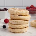 Two ingredient English muffins stacked on a marble board with fresh berries and jam on the side.