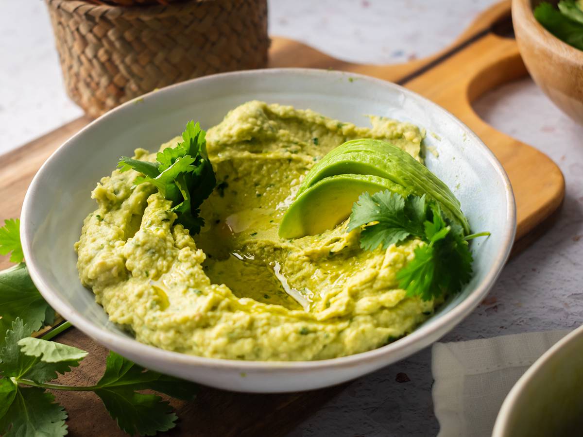 Avocado hummus in a bowl with cilantro and sliced fresh avocado.