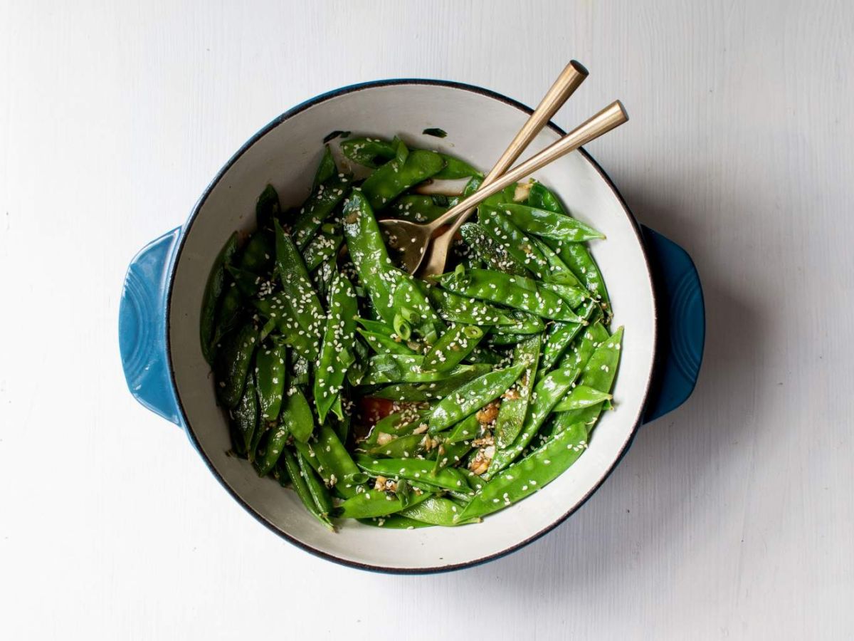 Sauteed snow peas with green onions, soy sauce, garlic, ginger, and sesame seeds with chopsticks.