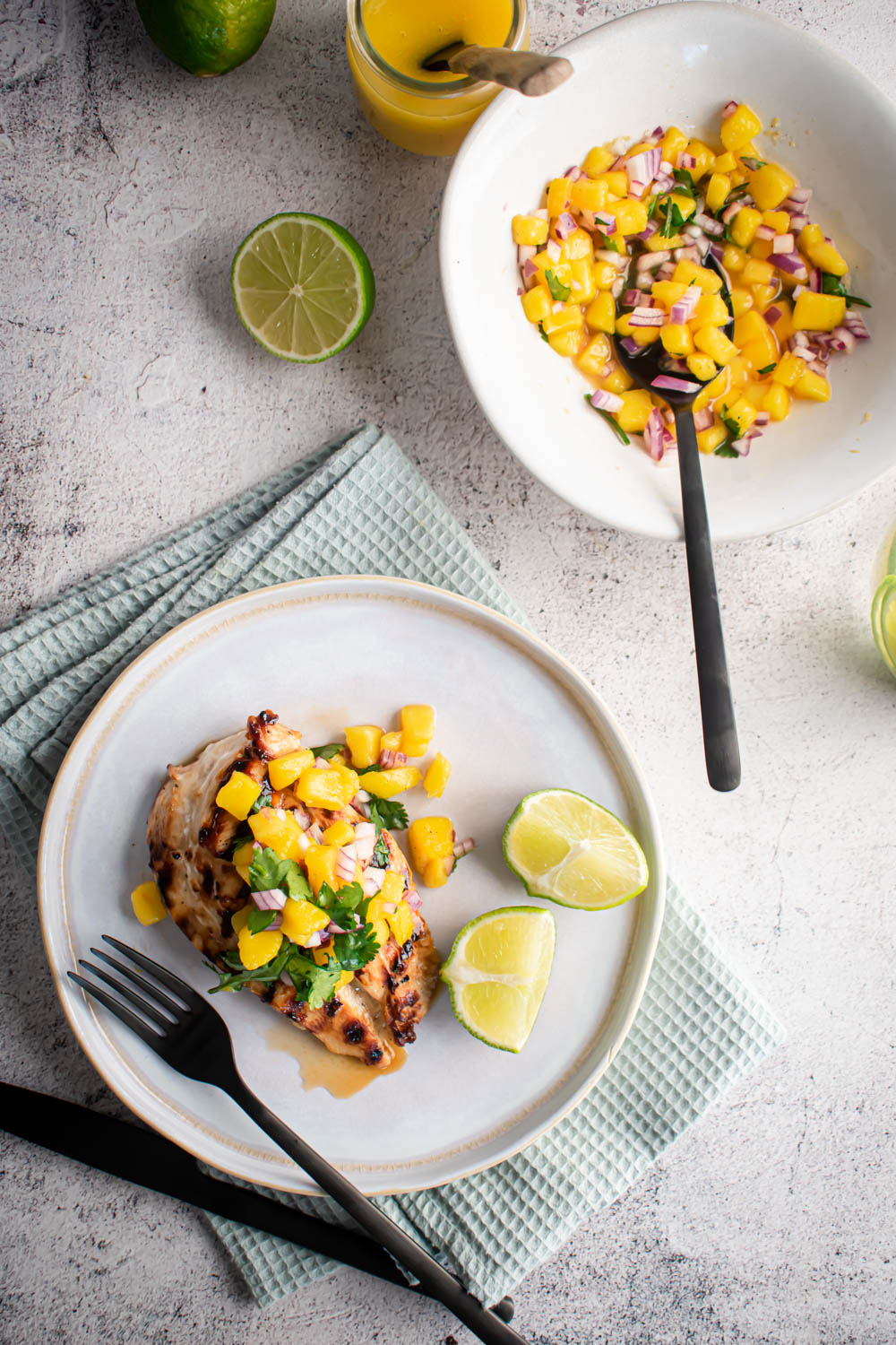 Mango salsa with grilled chicken breast served with extra salsa on the side and fresh lime wedges.