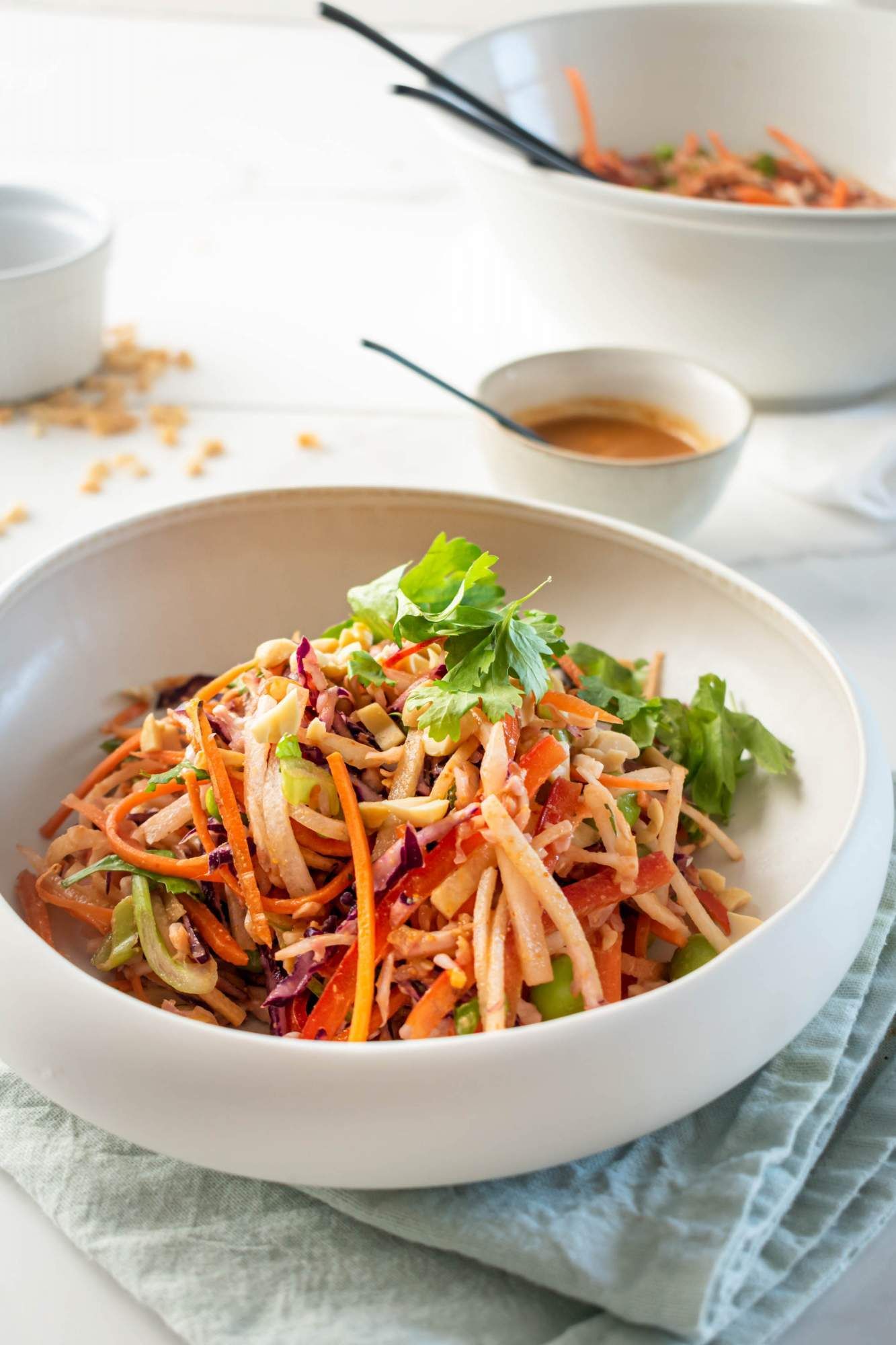 Peanut slaw made with shredded cabbage, carrots, red peppers, edamame, and onion in a bowl with dressing on the side.