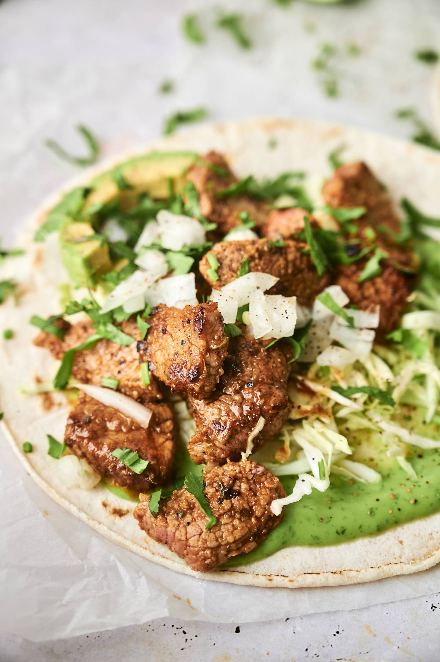 Tacos with carne asada, onions, cilantro, lime juice, and creamy salsa verde on a corn tortilla.