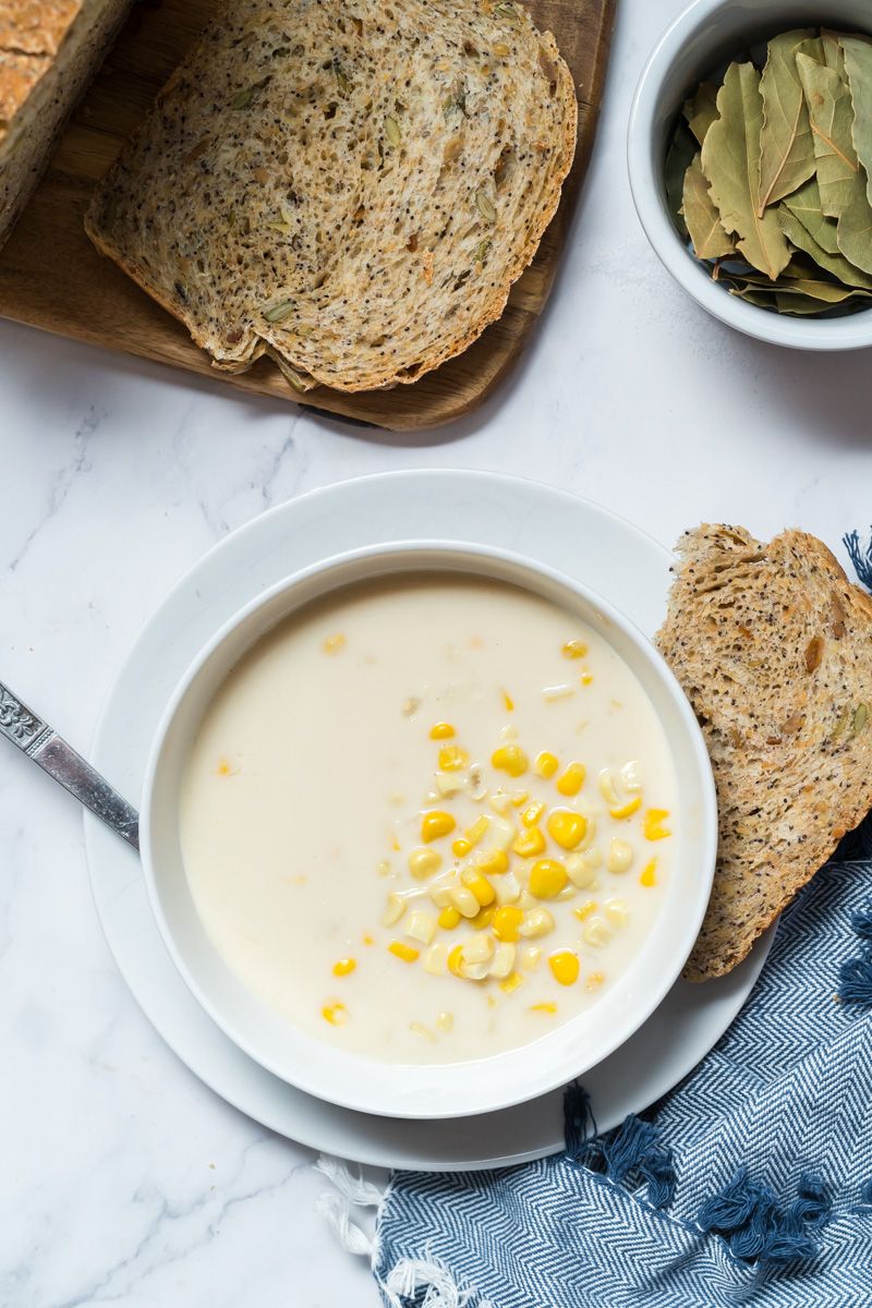 Corn and cauliflower chowder  in a bowl with wheat bread and bay leaves on the side.