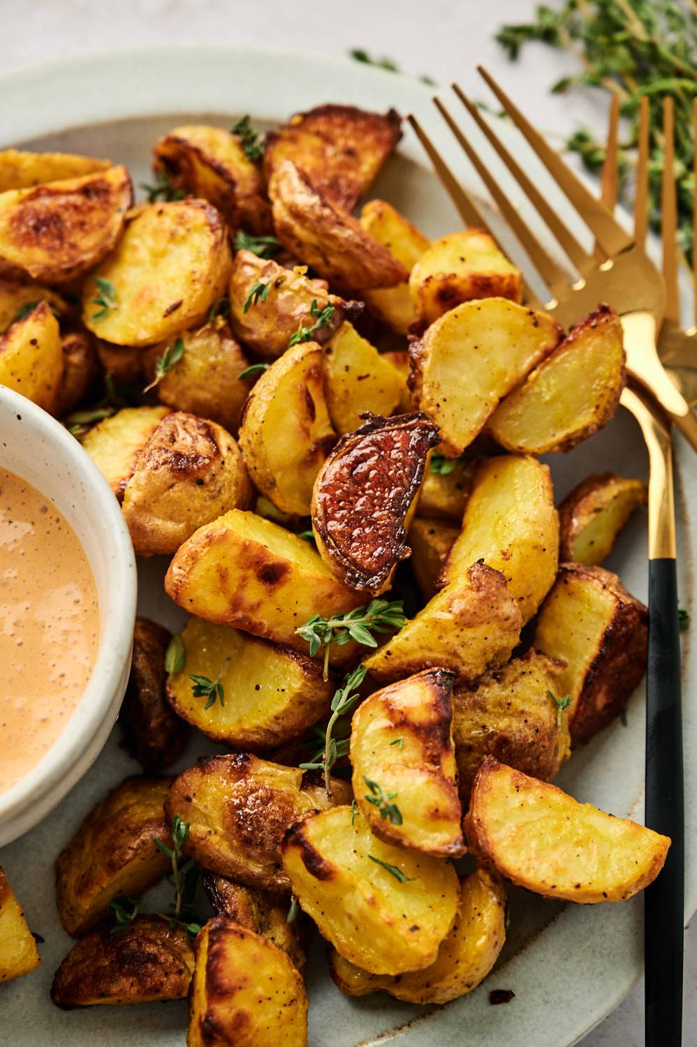 Roasted potatoes with browned crispy edges on a plate with thyme.