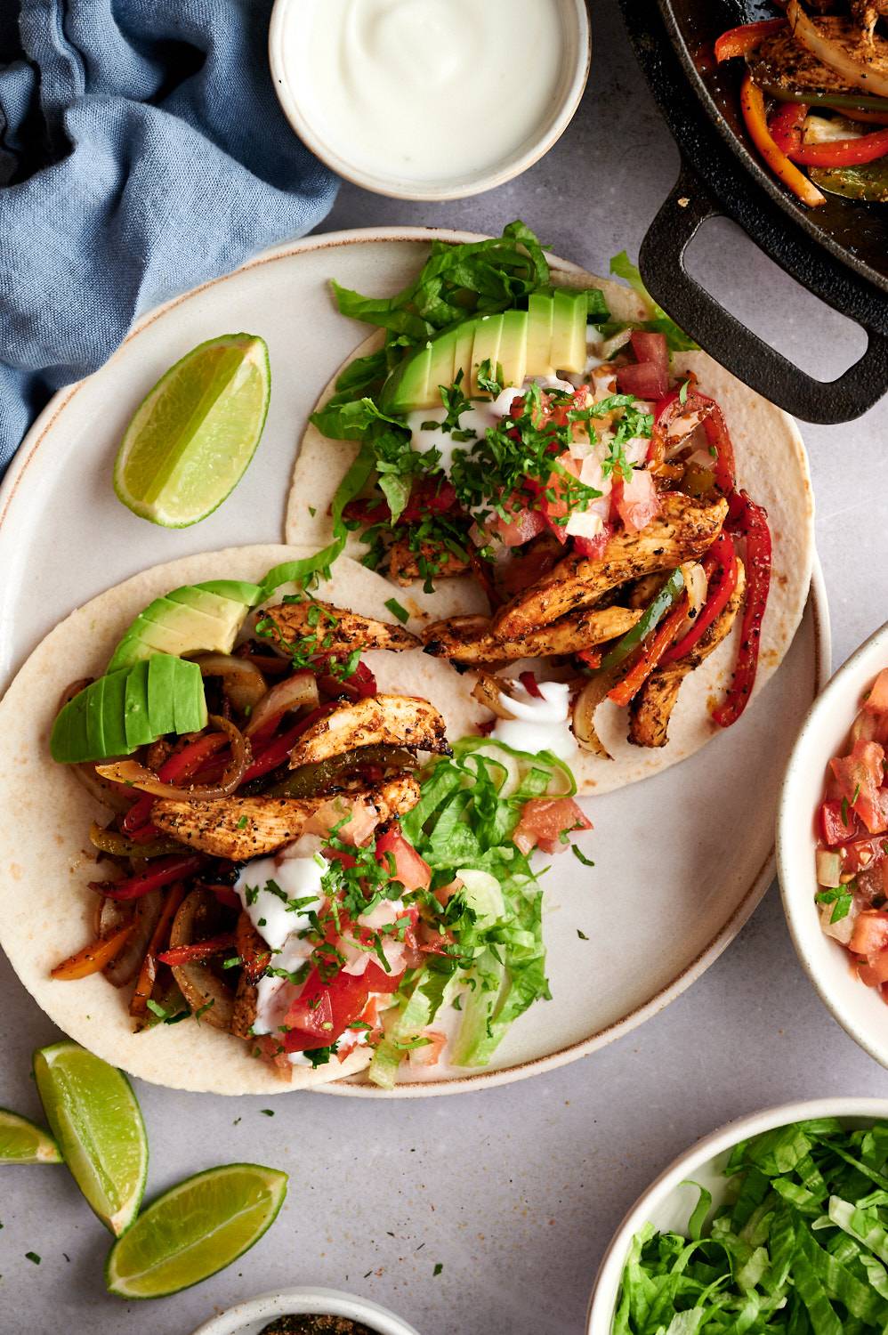 Easy fajita tacos with chicken, onions, peppers, avcoado, salsa, and sour cream in corn tortillas with a skillet on the side.