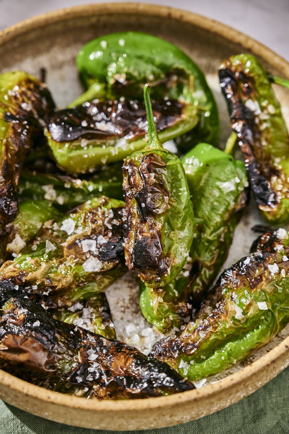 Blistered grilled shishito peppers served in a bowl with soy sauce and flkay sea salt.