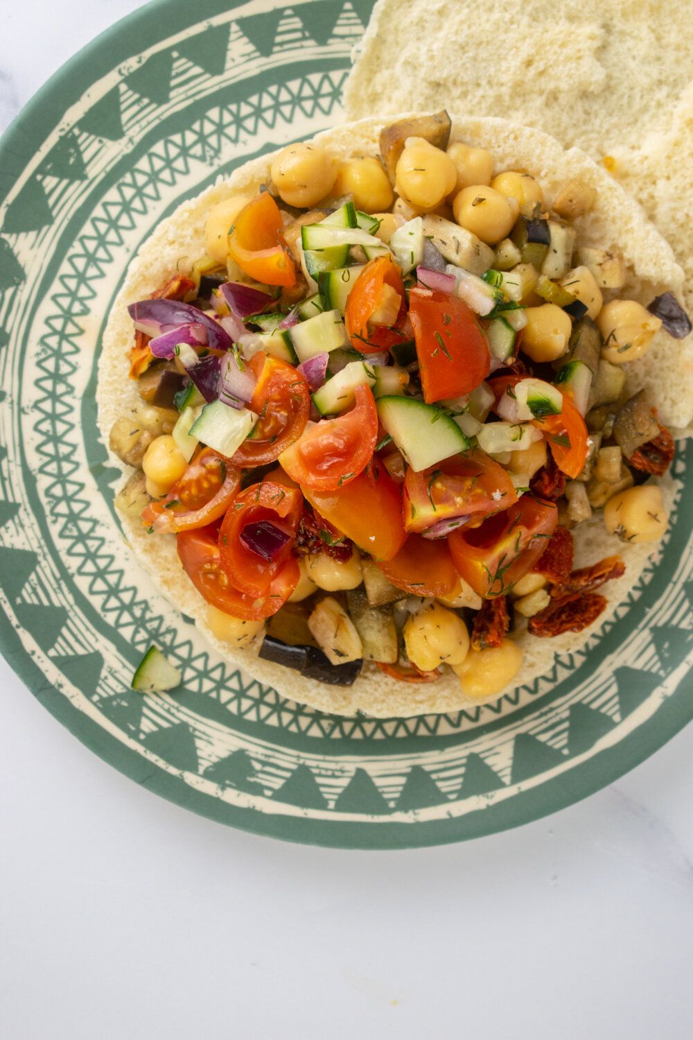 Greek eggplant tostadas with chickpeas, cucumbers, tomatoes, and red onions on a green plate.