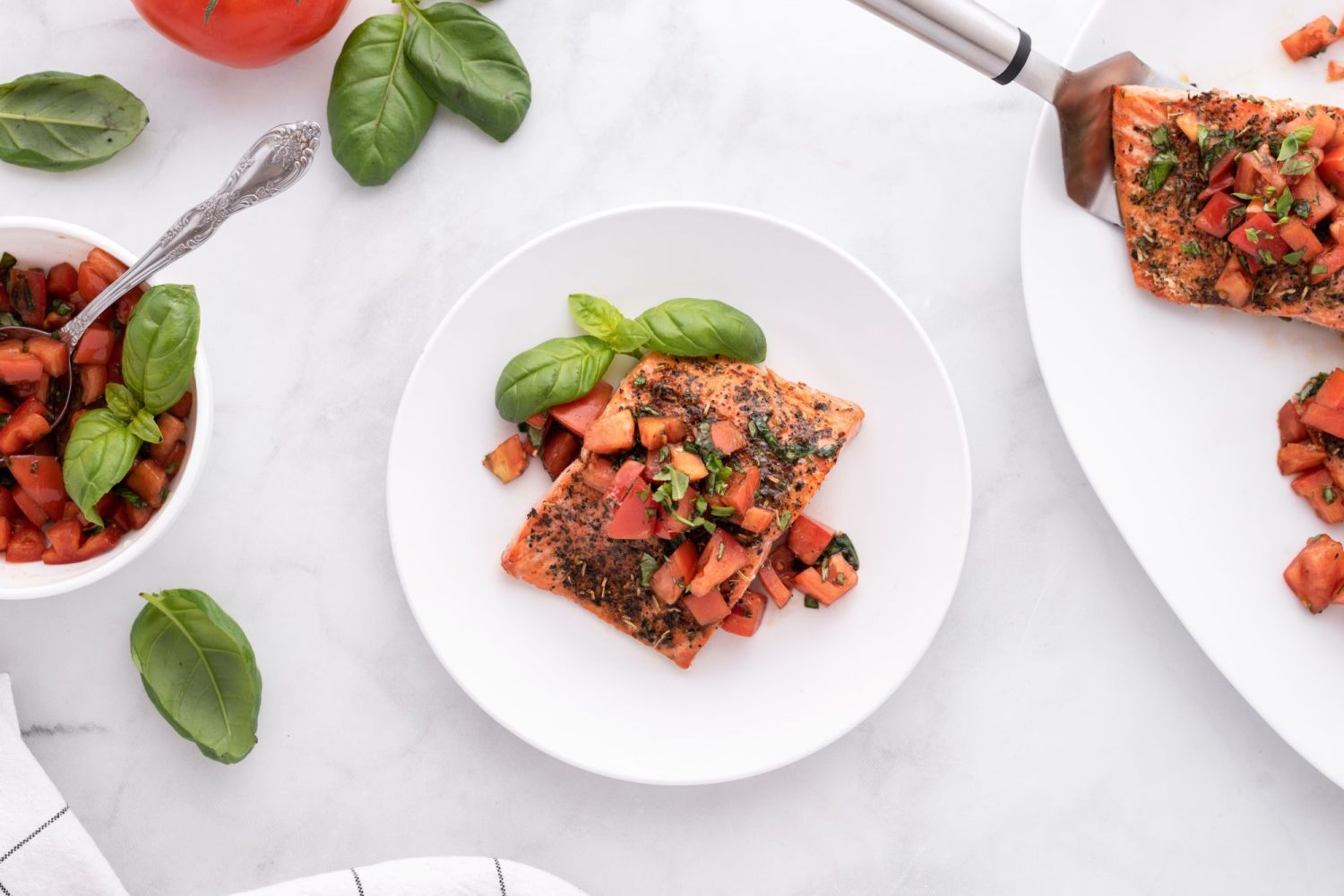 Italian salmon with tomato basil salsa on a white plate with tomatoes and basil leaves on the side.