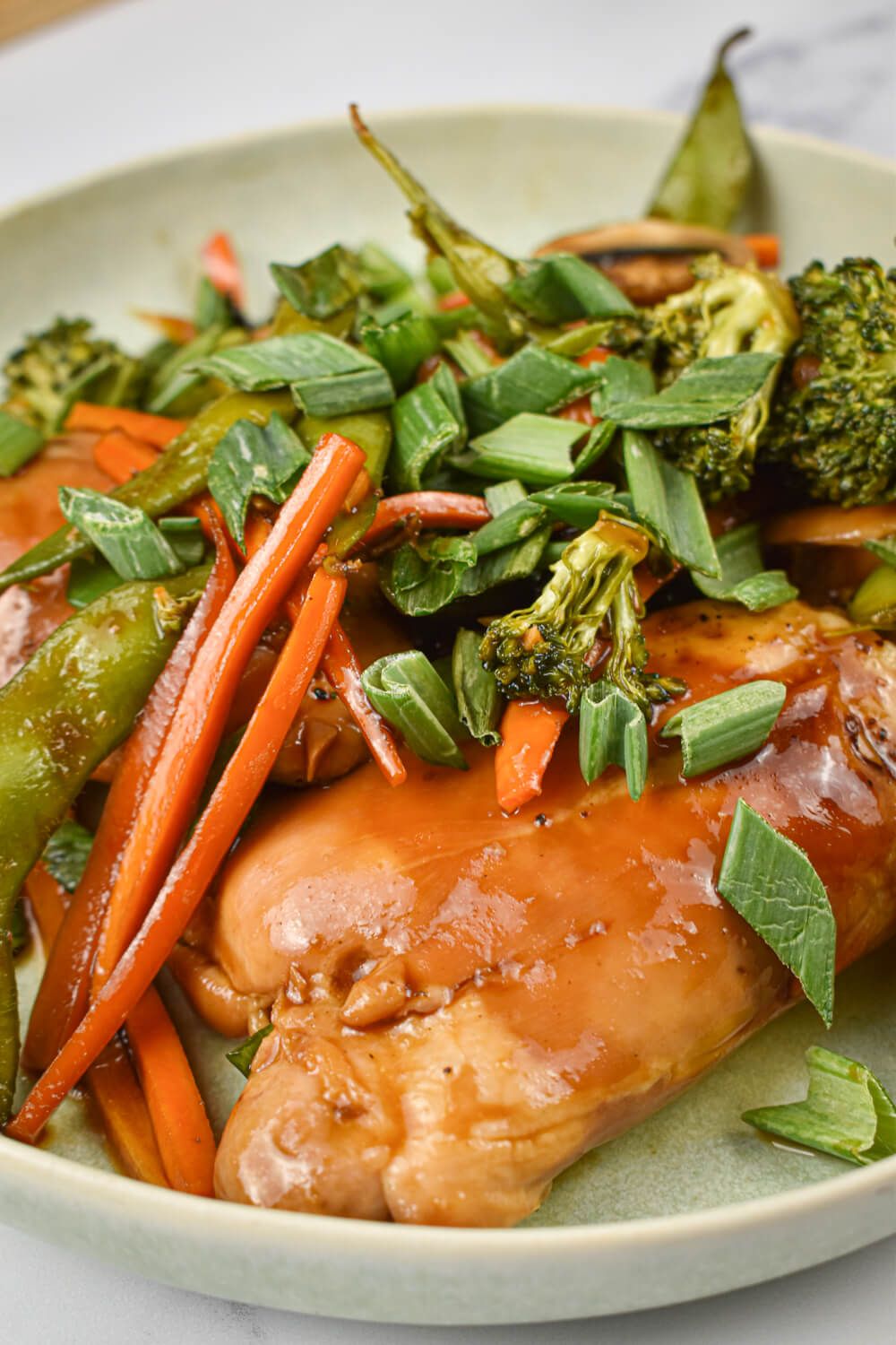 Teriyaki chicken and vegetables with chicken thighs, broccoli, carrots, sugar snap peas, and green onions.