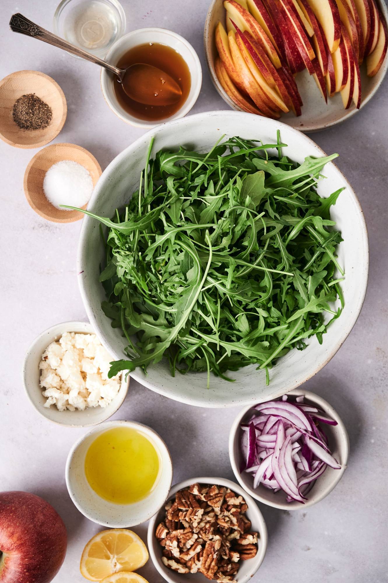 Ingredients for aragula and apple salad including fresh baby arugula, apples, red onions, lemon juice, honey, vinegar, and spices.