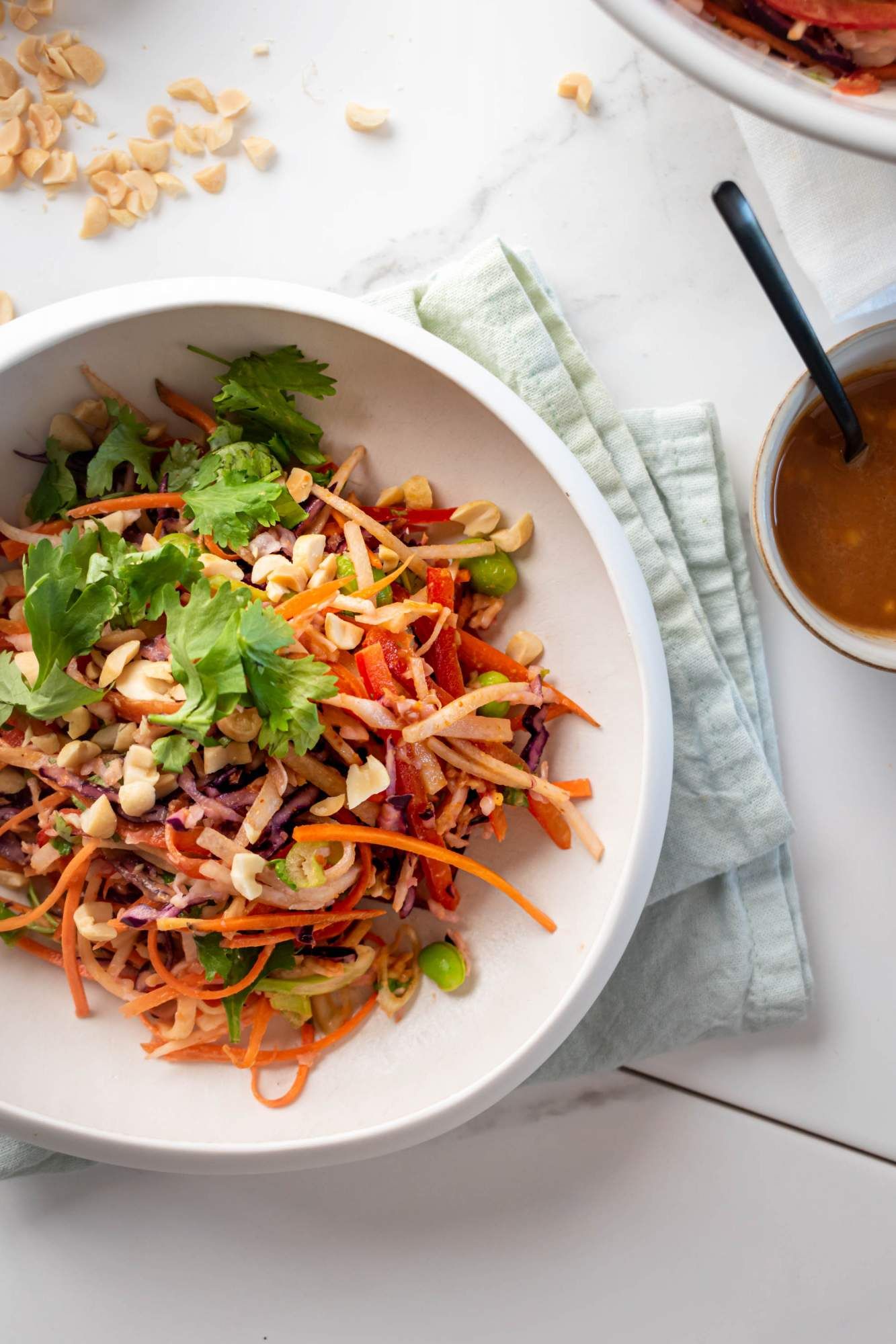 Asian slaw with cababge, carrots, edamame, and green onions tossed in a peanut lime dressing in a large bowl.