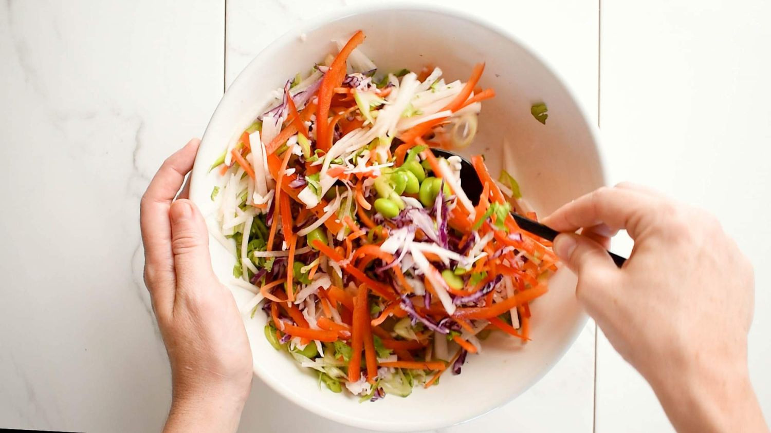 Bowl with cabbage slaw, red peppers, edamame, green onions, and cilantro being stirred.