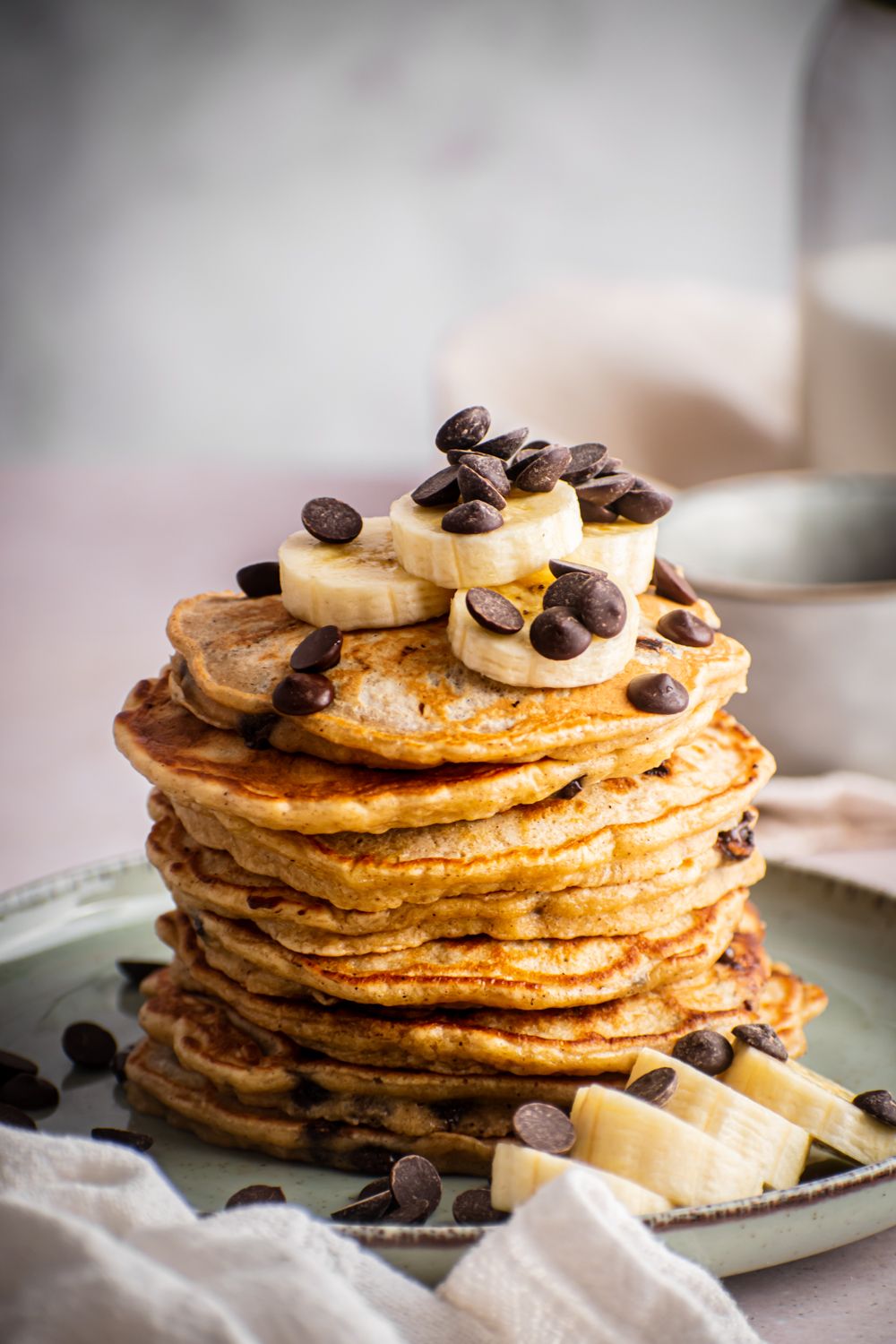 Chocolate chip banana pancakes stacked on a plate with extra banana slices and chocolate chips on top.