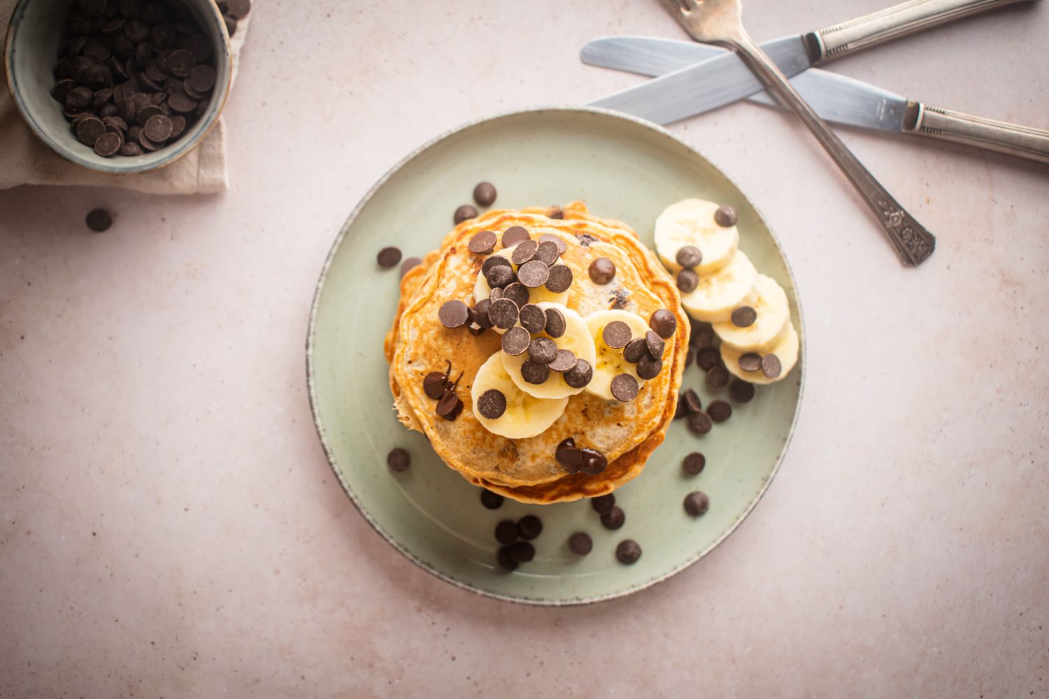 Pancakes with bananas and chocolate chips on a plate with chocolate chips on the side.