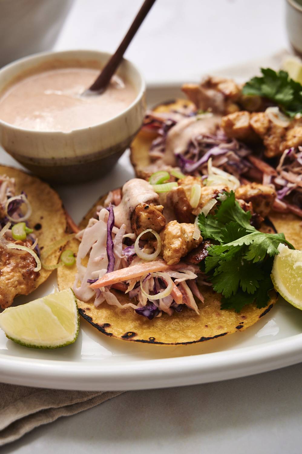 Chicken tacos with bang bang sauce, creamy slaw, cilantro, and lime served on corn tortillas.