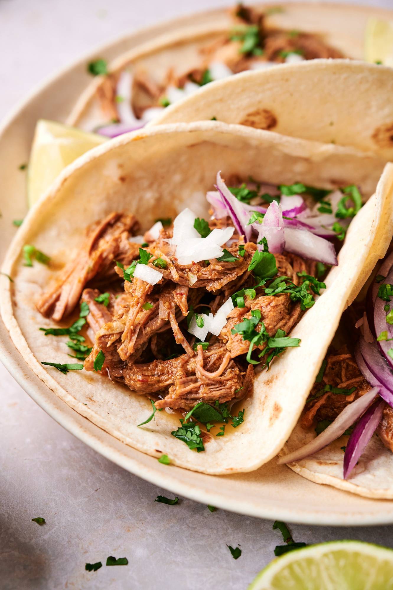 Barbacoa beef tacos with red onion, cilantro, and lime wedges served in corn toritllas.