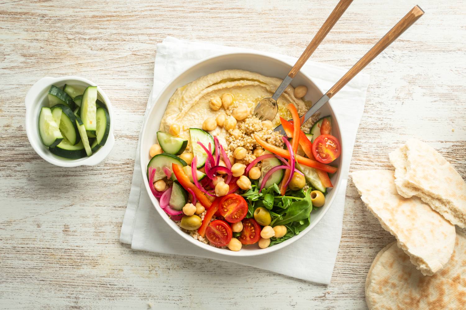 Hummus grain bowl with chickpeas, hummus, tomatoes, cucumbers, red onions, and greens.