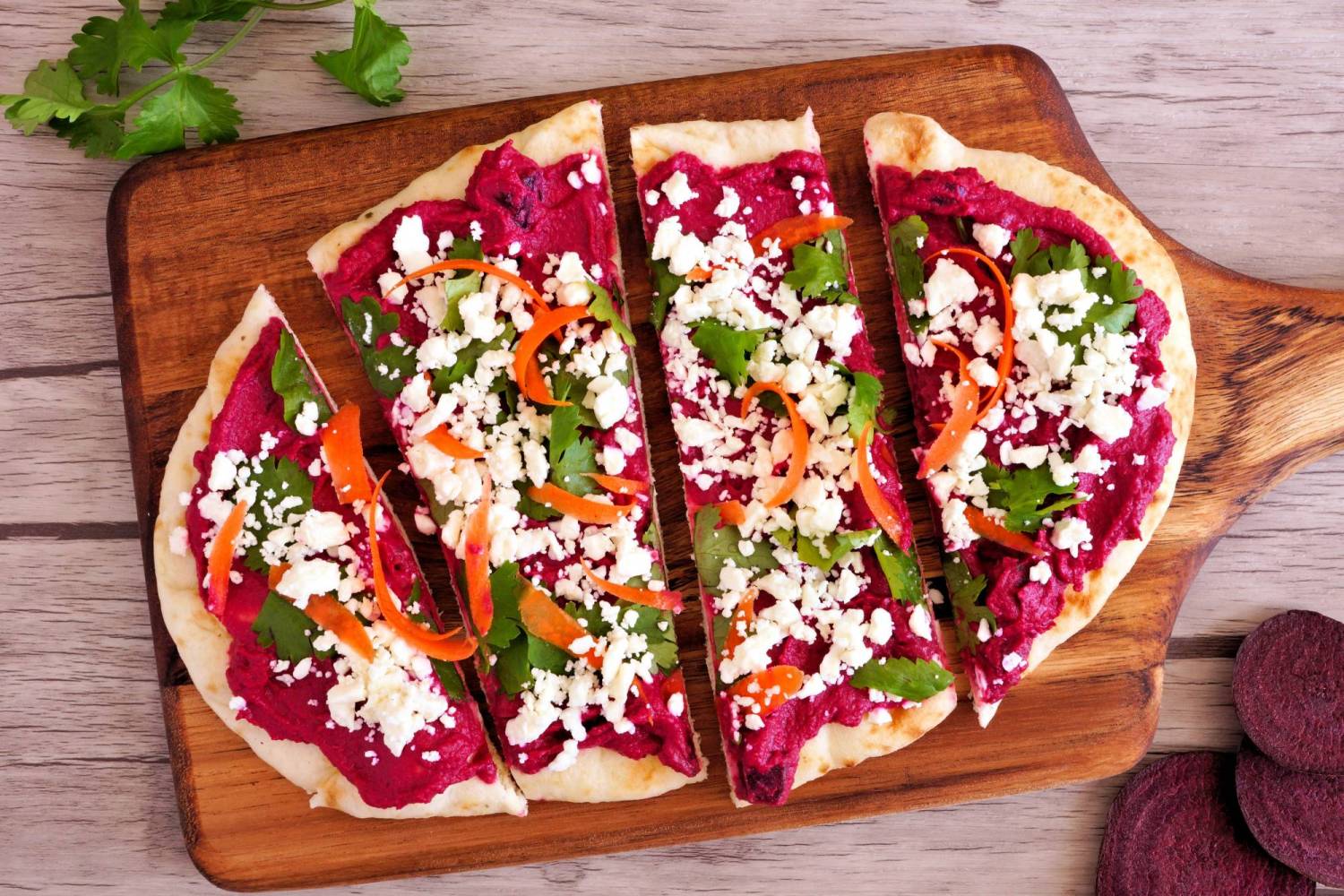 Beet hummus flatbread with cilantro, carrots, and feta cheese.