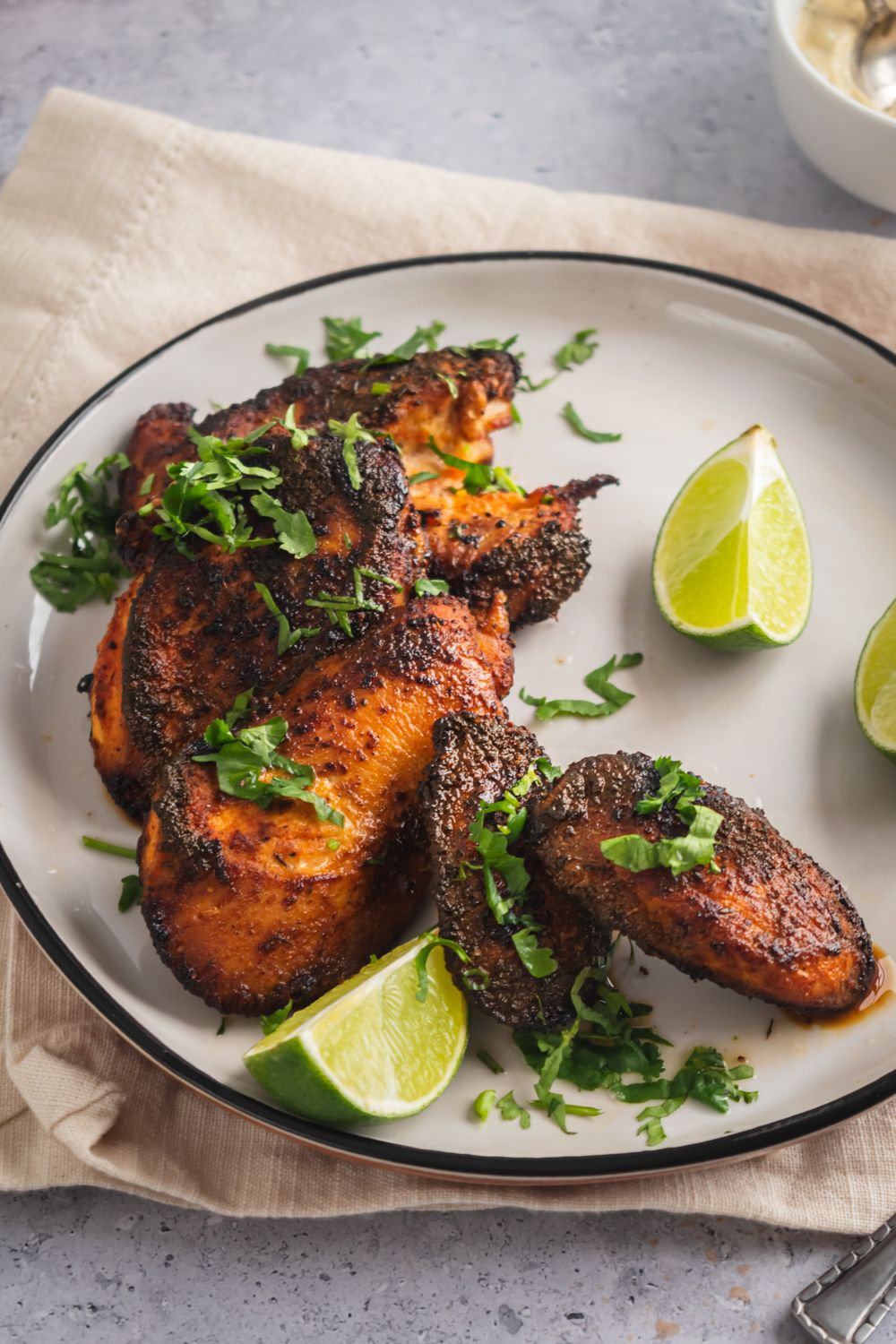 Chicken breast coated in blackening seasoning on a plate with lime edges and herbs.