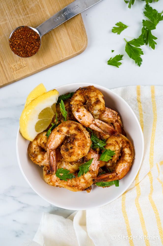 Easy Cajun spiced shrimp in a bowl with fresh lemon slices and parsley and Cajun seasoning on the side.