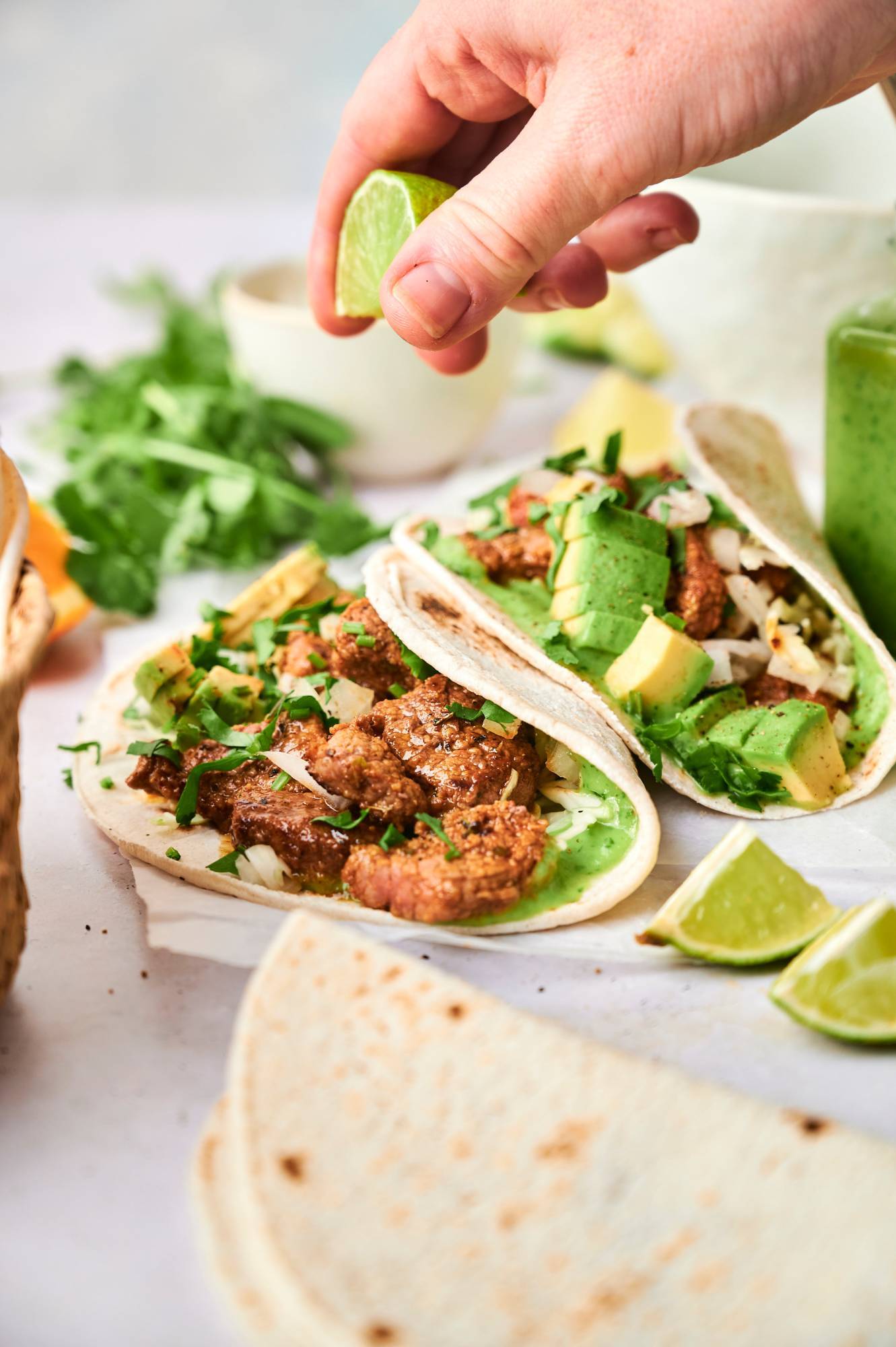 Street tacos with carne asada served in warm tortillas with avocado, cilantro, onion, and fresh lime juice being squeezed on top.