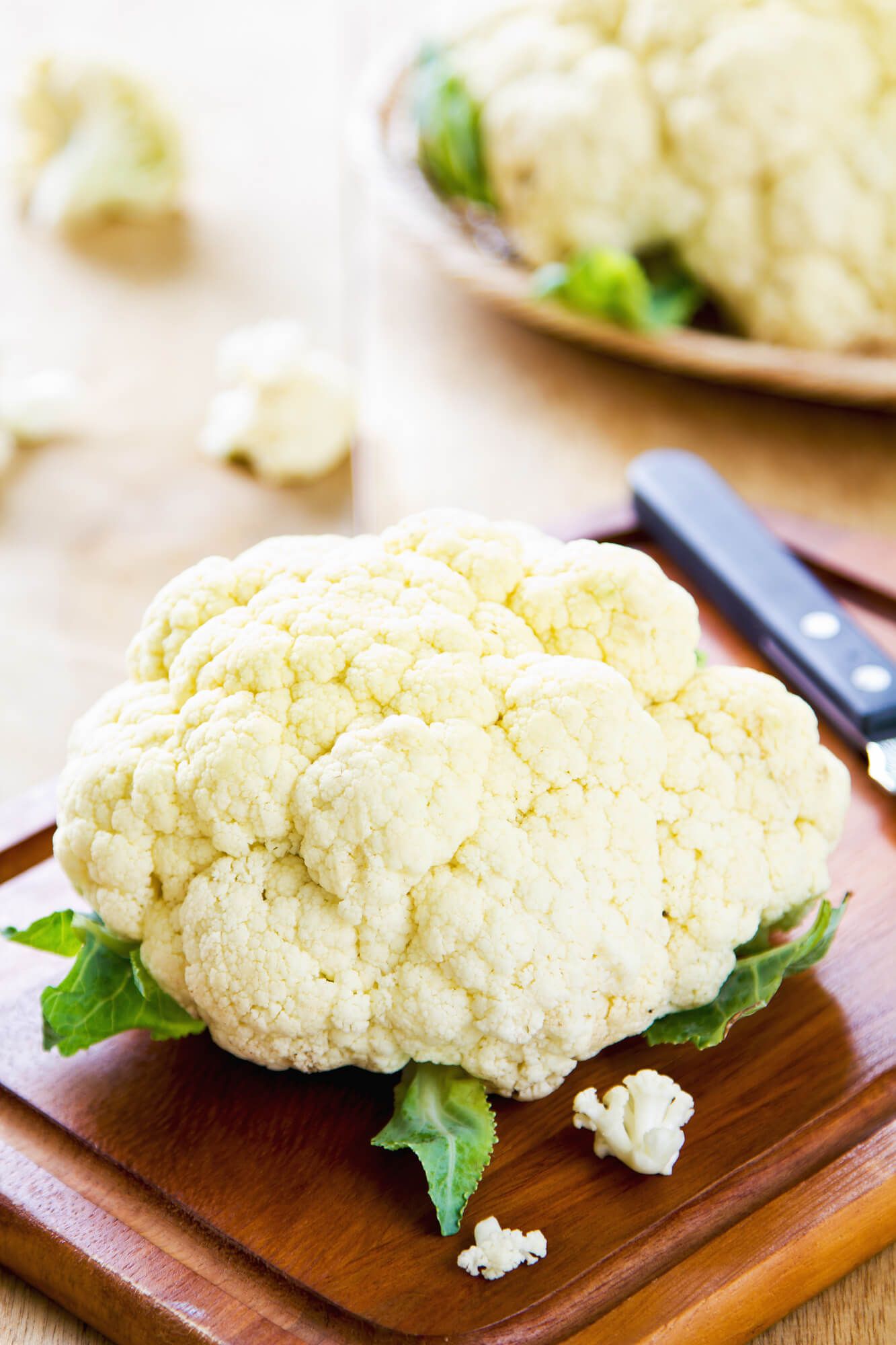 Cauliflower on a cutting board with a knife and some florets.