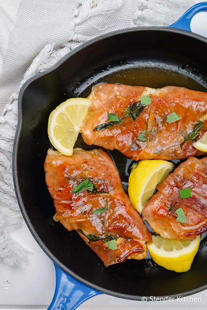 Chicken Saltimbocca in a skillet wrapped in prosciutto with sage and lemon.