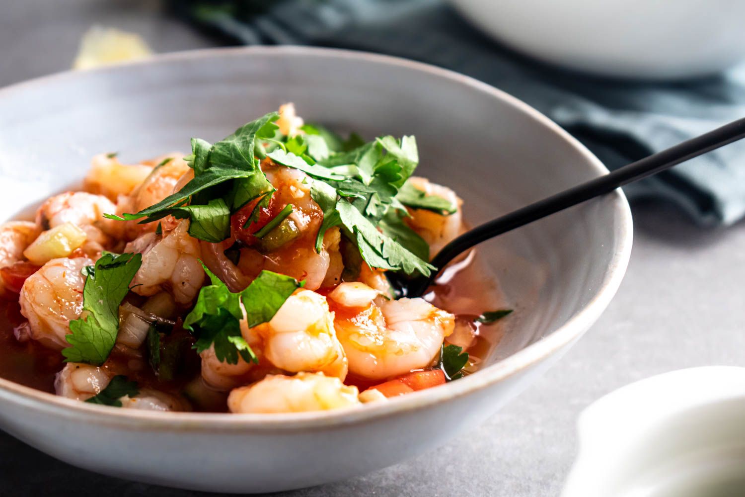 Mexican shrimp cocktail served in a white bowl with shrimp in a Mexican tomato sauce with onions, cucumbers, and cilantro.