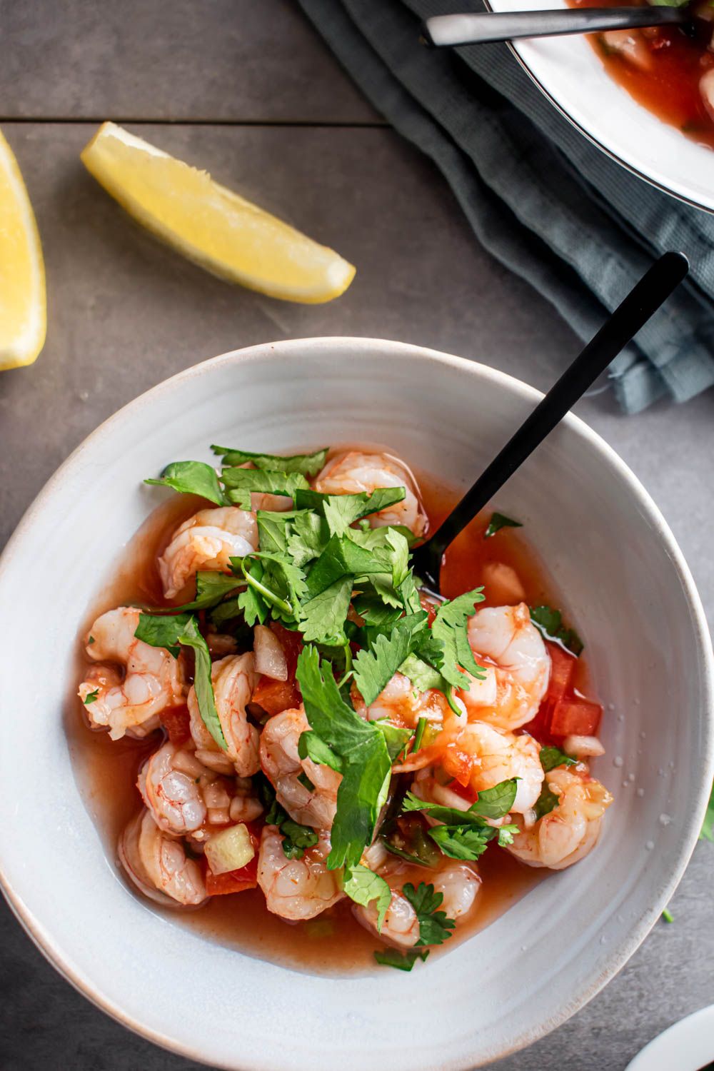 Homemade coctel de camarones, Mexican shrimp cocktail, served in a white bowl with cilantro and limes.