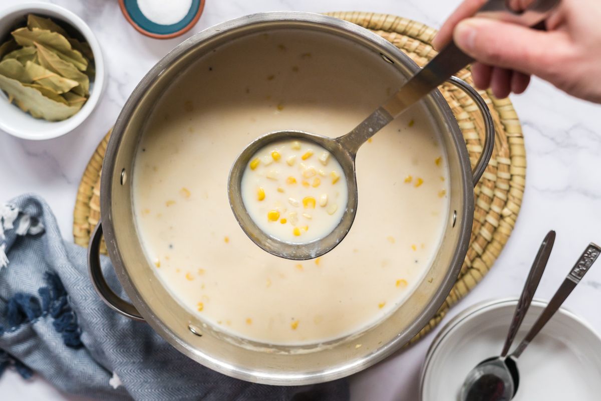 Lightened up corn chowder with cauliflower being scooped out of a soup pot.