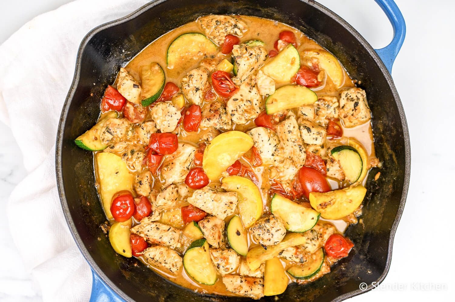 Creamy tuscan chicken in a skillet with vegetables and Parmesan cheese.