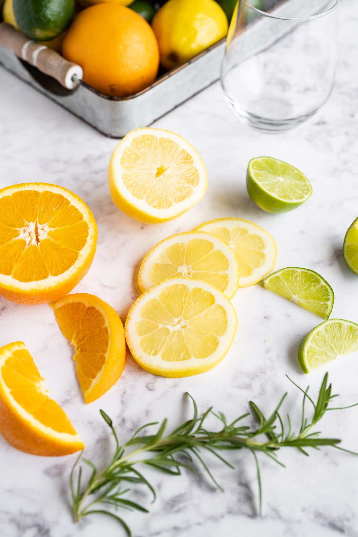 Ingredients to make citrus detox eater on a marble board with fresh limes, oranges, lemons, and herbs.