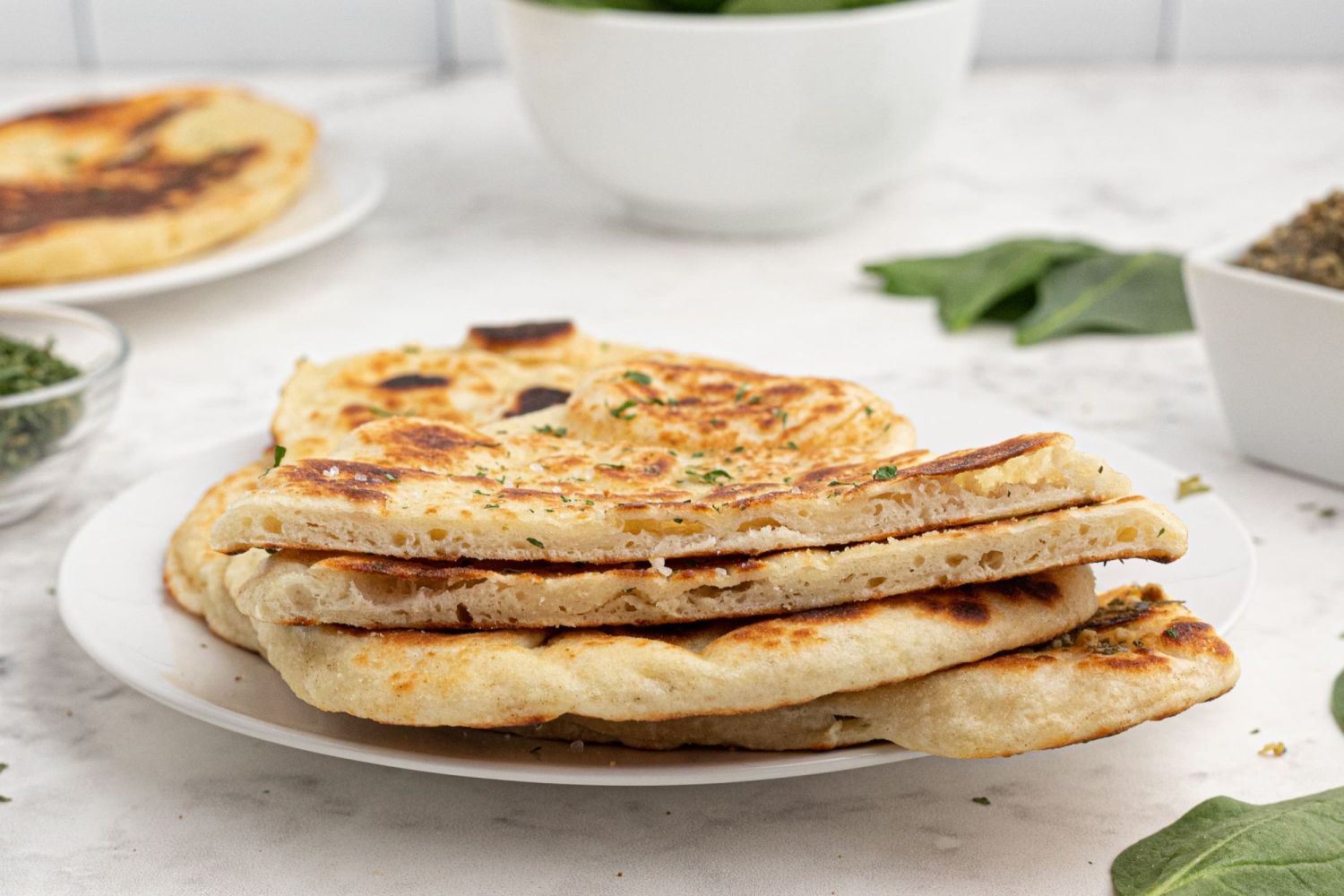 Indian Naan bread cut in half and sprinkled with garlic salt and herbs on a plate with chutney on the side.