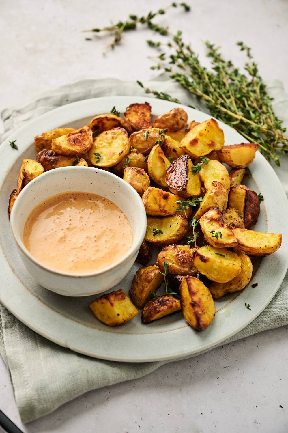 Mustard roasted potatoes on a plate with dipping sauce and fresh herbs.