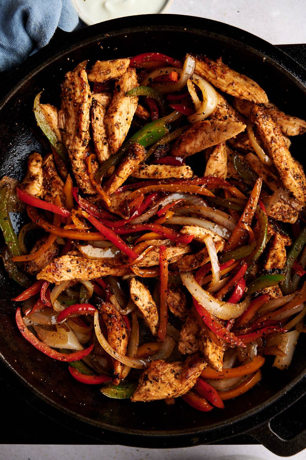 Chicken fajita taco filling with sliced chicken breast, bell peppers, onions, and seasoning in a cast iron skillet.