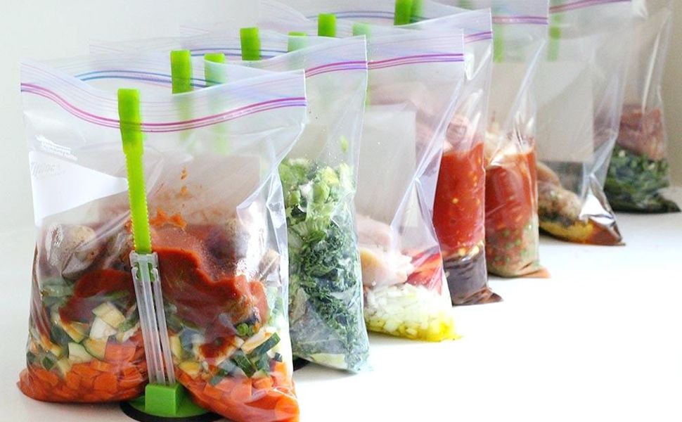 Freezer siorage bags with vegetables and sauce being held up by freezer bag clips.