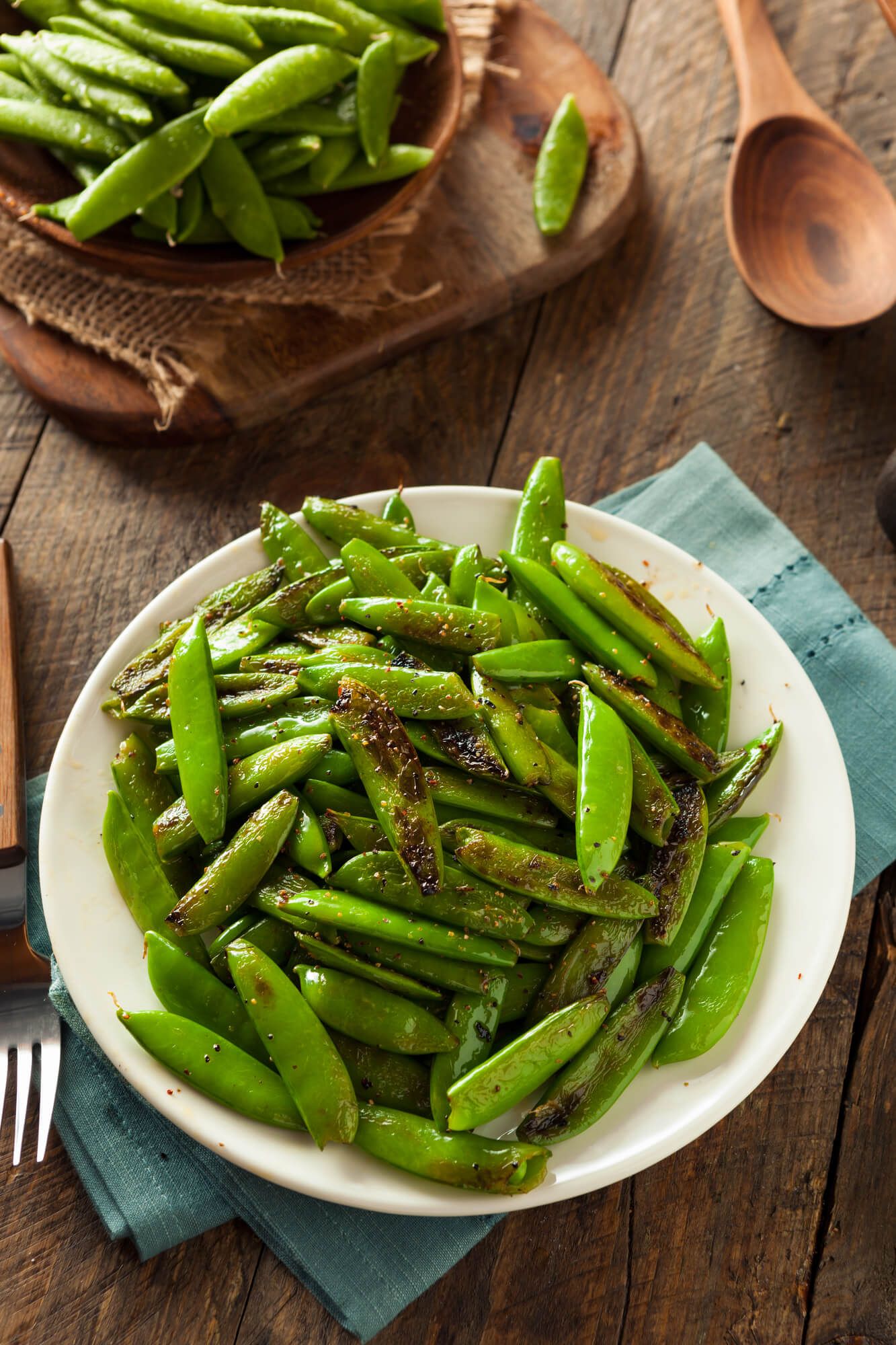 Snap pea recipe cooked on a wooded plate with a napkin.