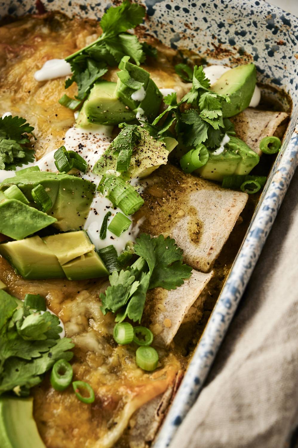 Baked green chicken enchiladas topped with avocado, cilantro, green onions, and sour cream.