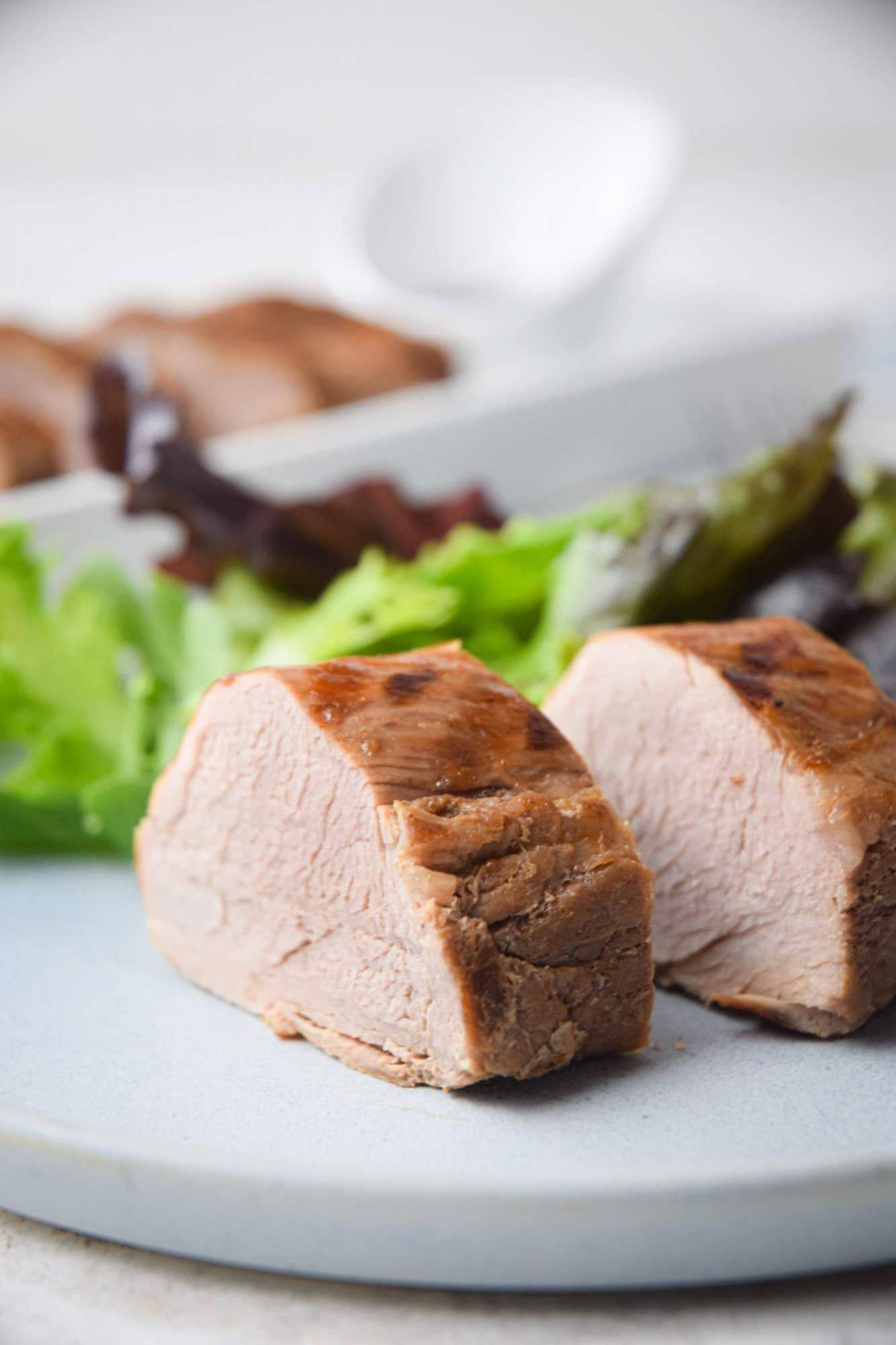 Grilled pork tenderloin with hoisin sauce on a plate with sesame seeds and greens.