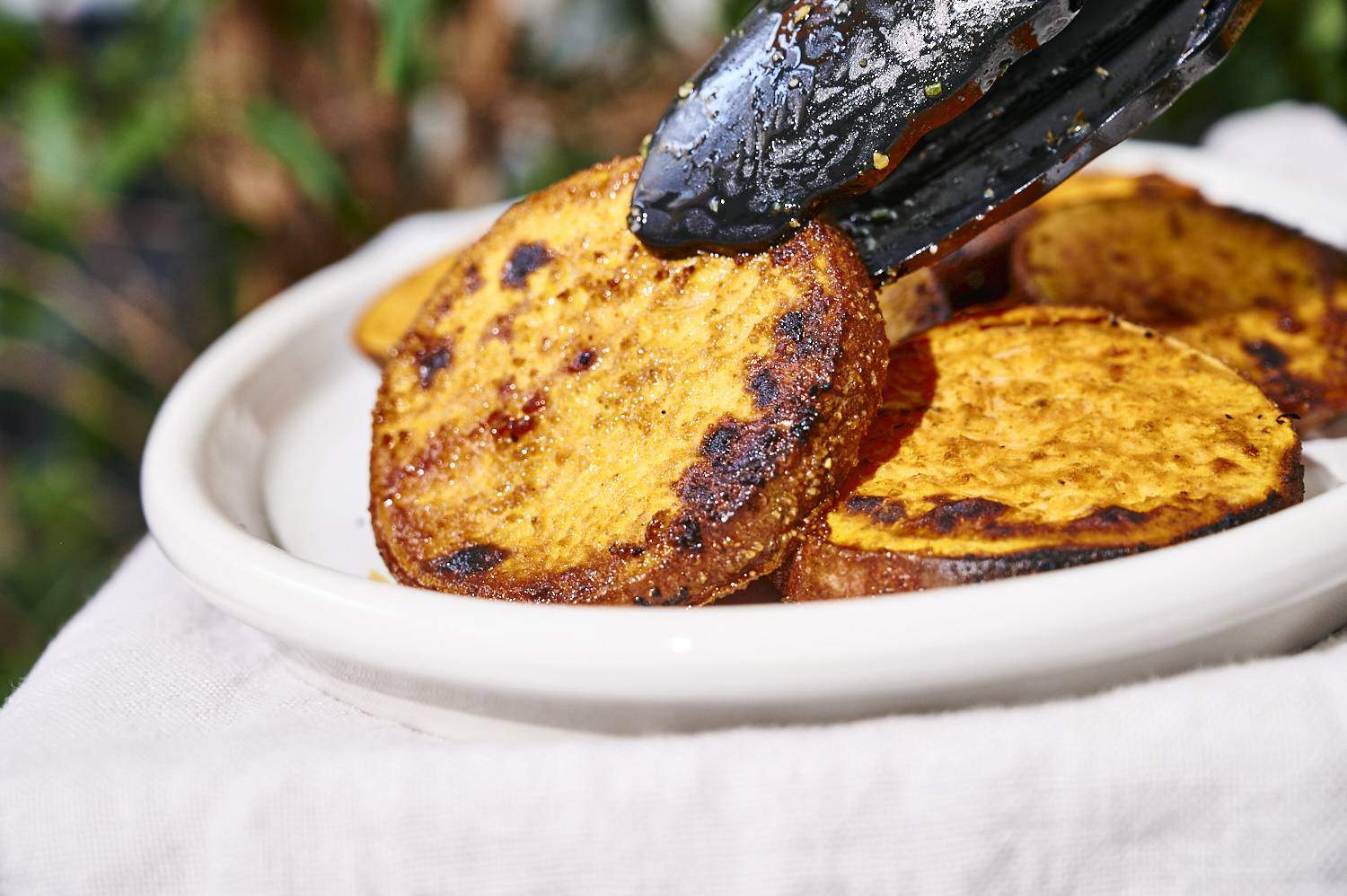 Tongs picking up caramelized grill sweet potatoes.