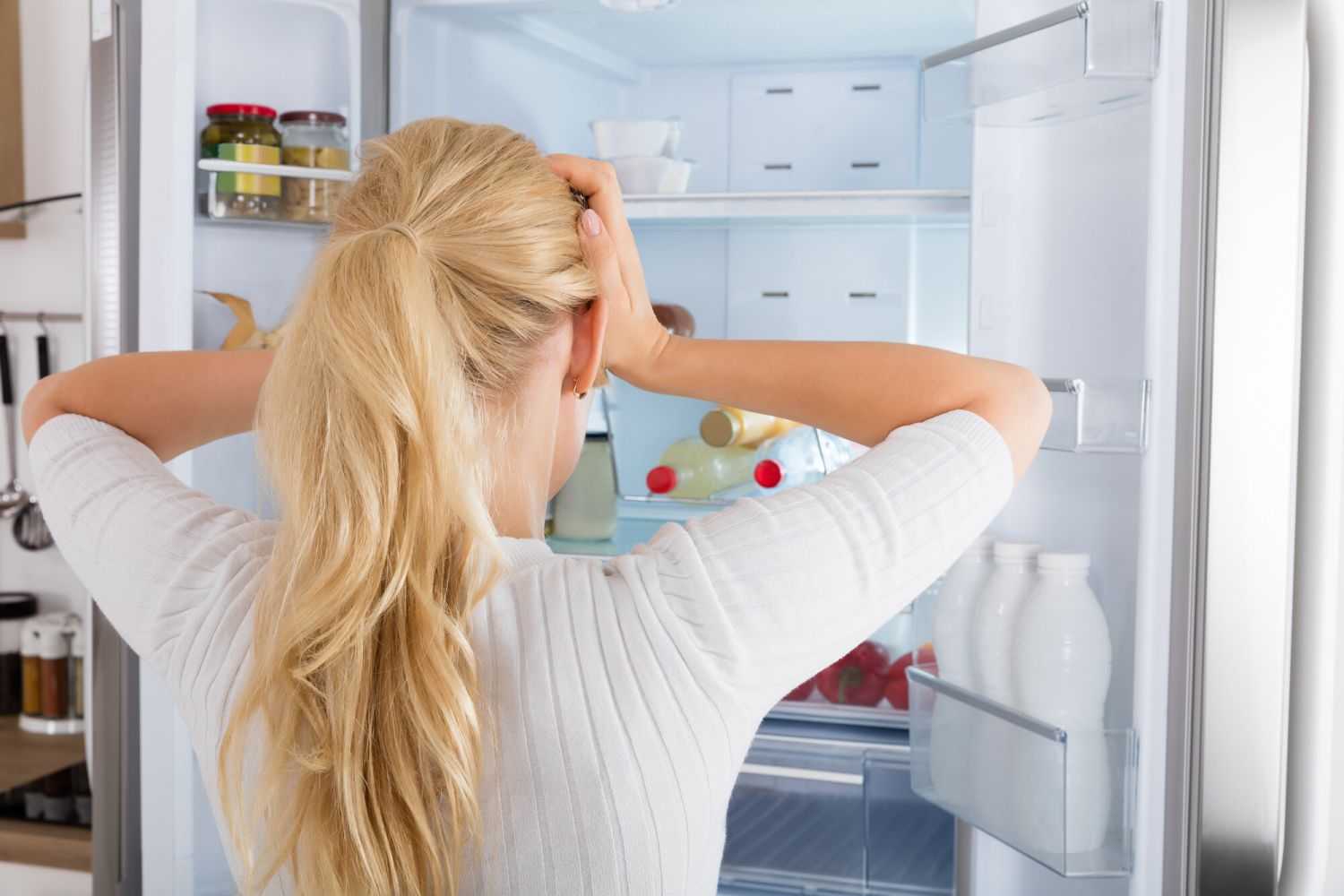 Woman looking into fridge with hands on head trying to figure out what to eat.
