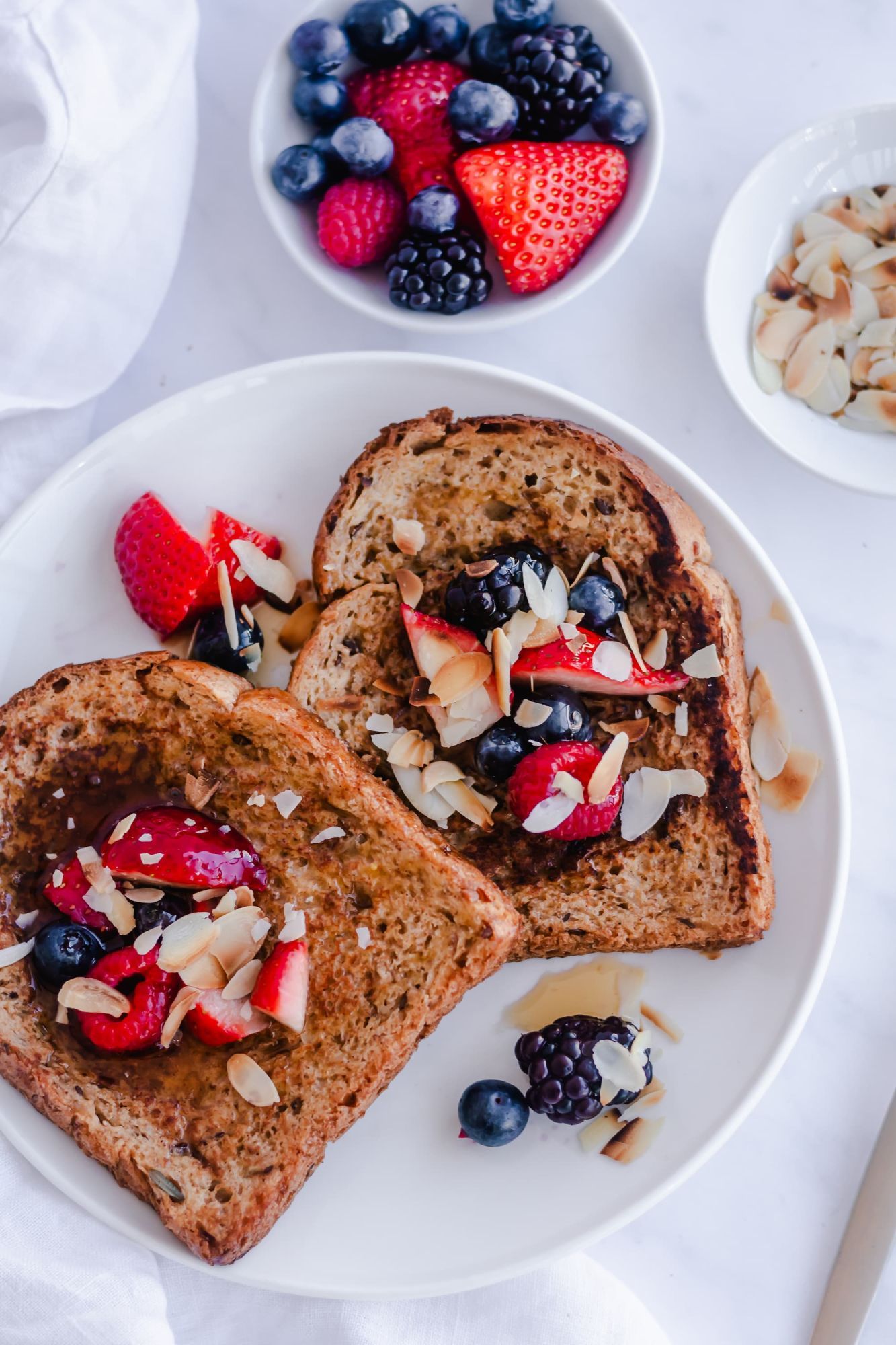 Whole grain French toast topped with strawberries, blackberries, almonds, coconut, and syrup.