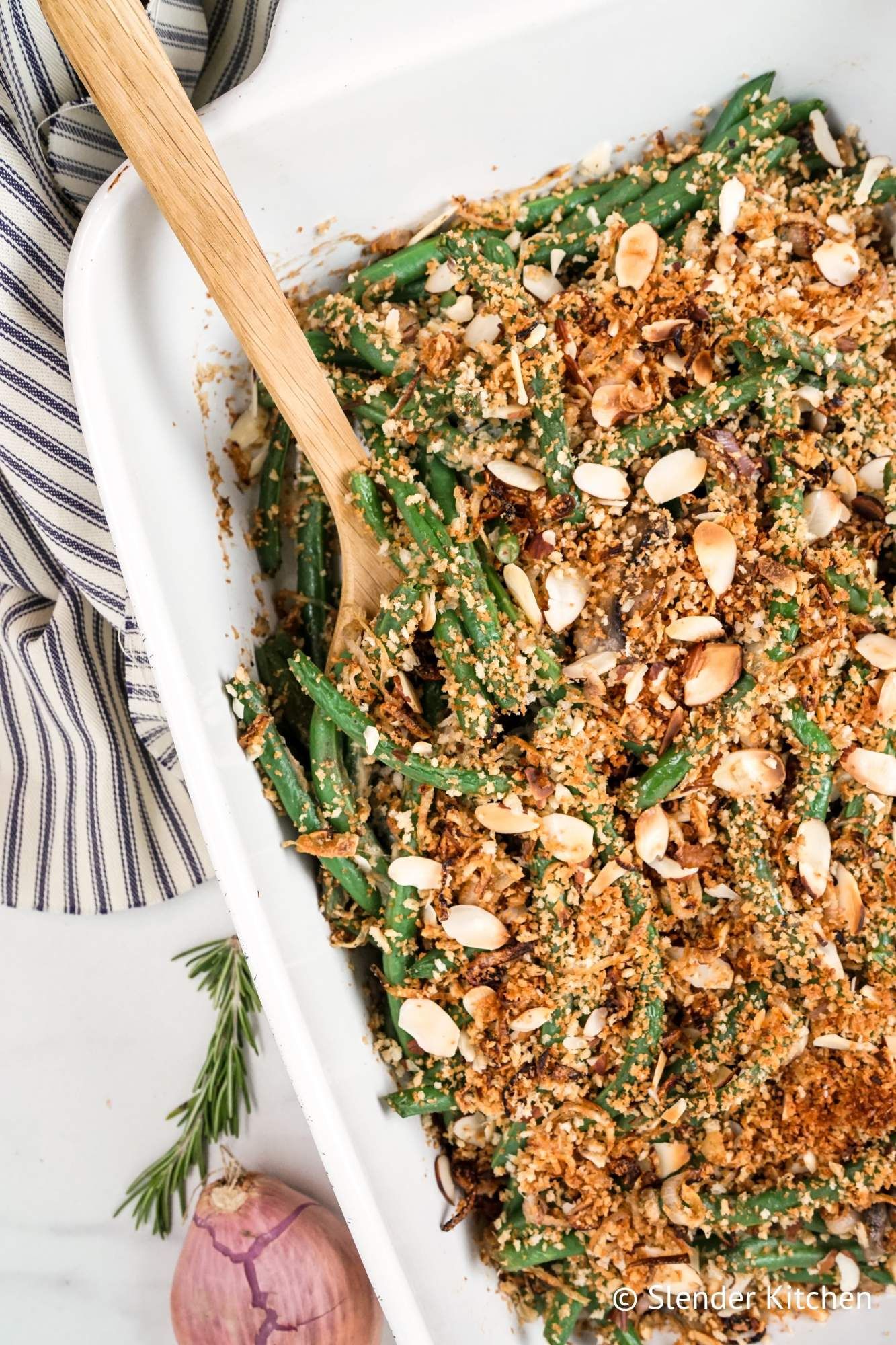 Healthy green bean casserole with crispy onions and almonds in a baking dish with a wooden spoon.