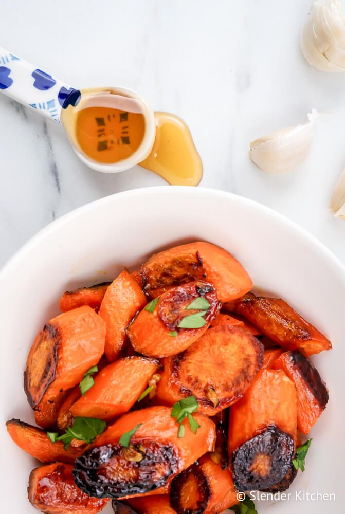 Honey Roasted carrots with a spoon of honey and loose garlic cloves on the side.